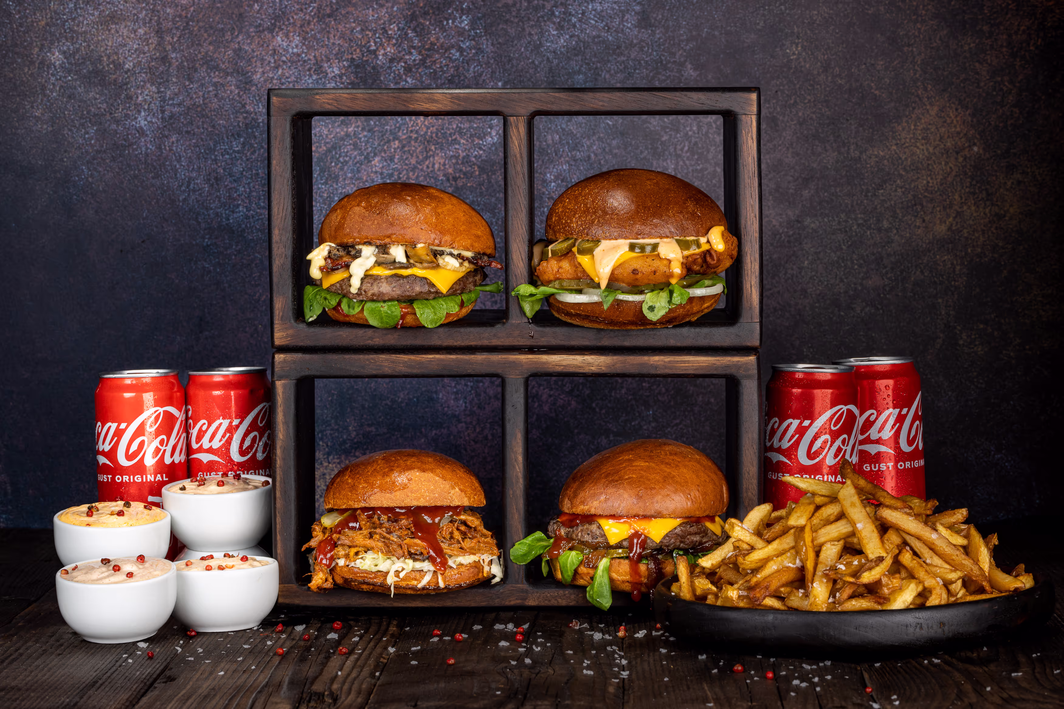 Un sortiment de burgeri acompaniați de o porție de cartofi prăjiți și Coca-Cola.