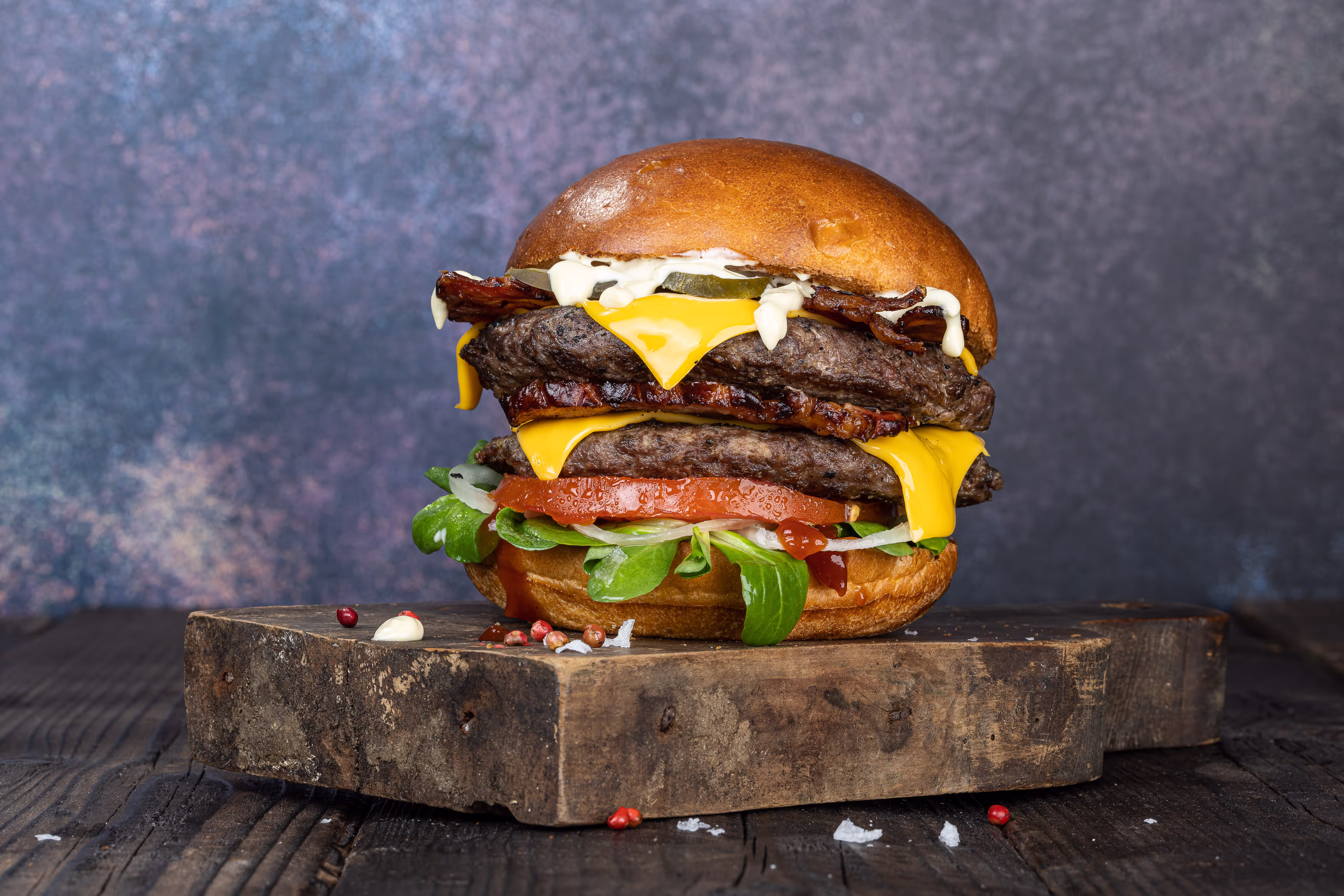 Un burger cu două straturi suculente de carne de vită, bacon crocant, brânză Cheddar topită și legume proaspete, servit într-o chiflă pufoasă.