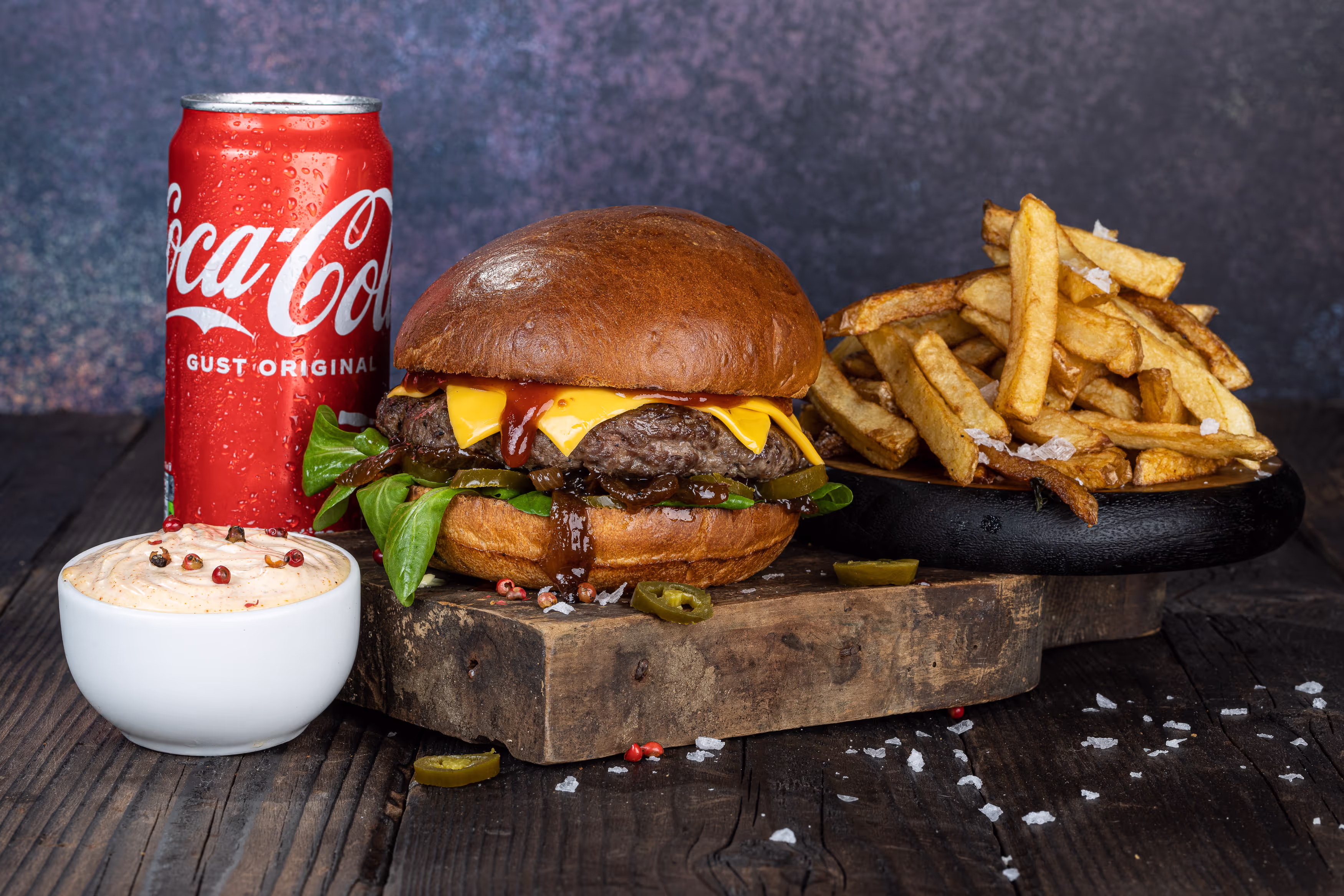 Burger premium cu carne suculentă de vită, brânză Cheddar topită și sos BBQ, alături de cartofi prăjiți crocanți și o Coca-Cola rece.
