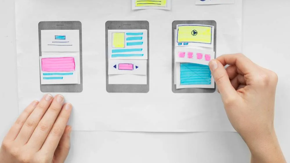 Hands arranging paper mobile wireframes