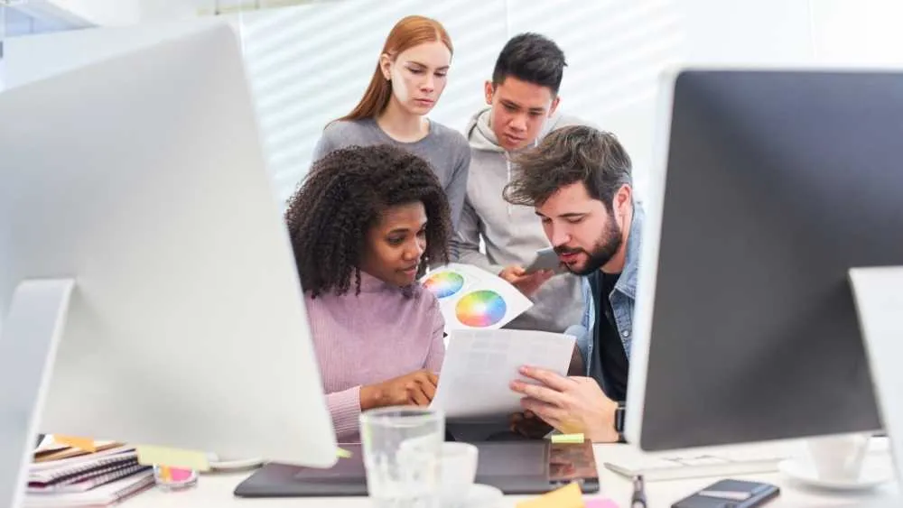 Team reviewing a chart together beside desktop computers