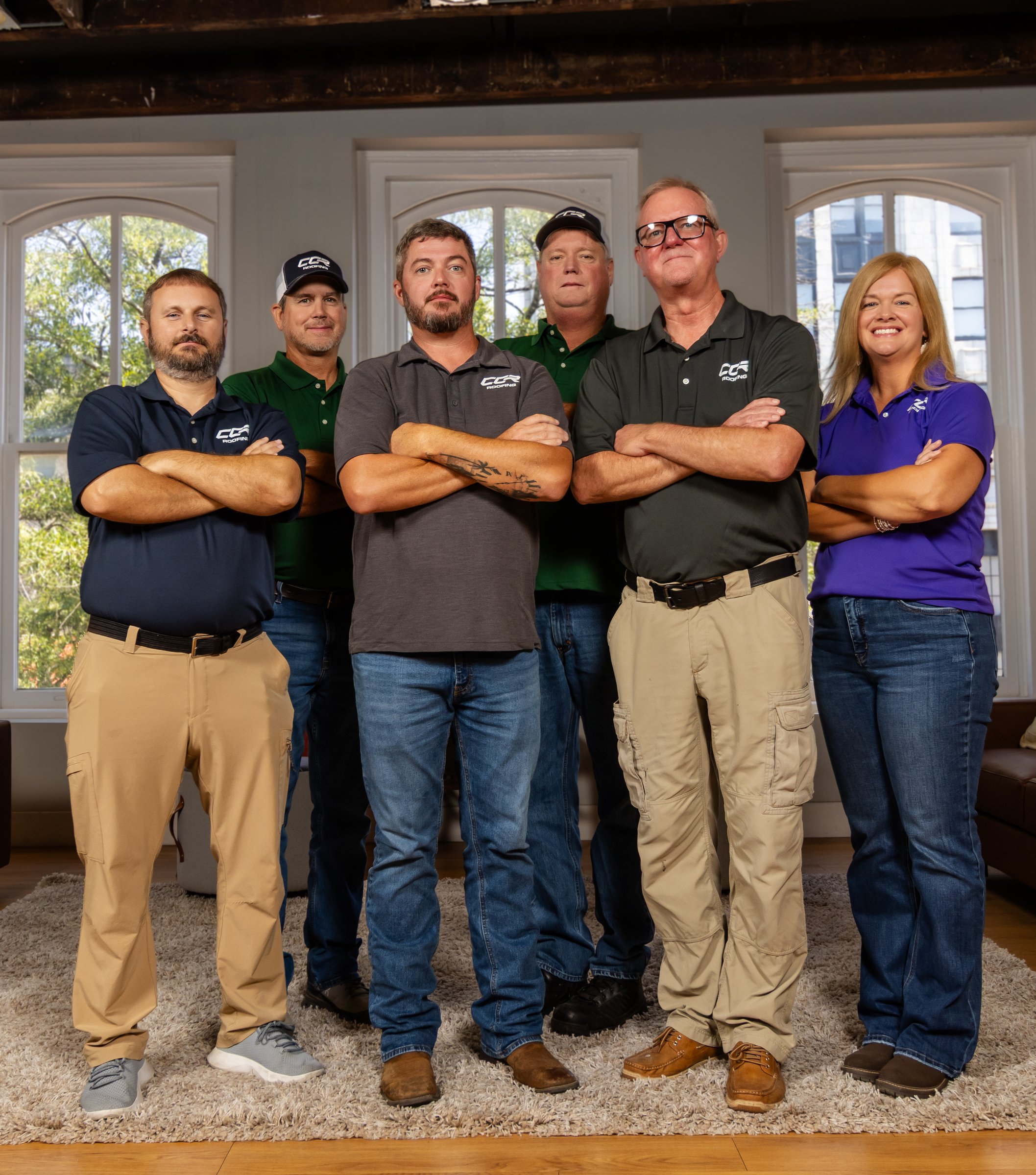 The CCR Roofing team of six standing together indoors, arms folded, in CCR branded polo shirts.