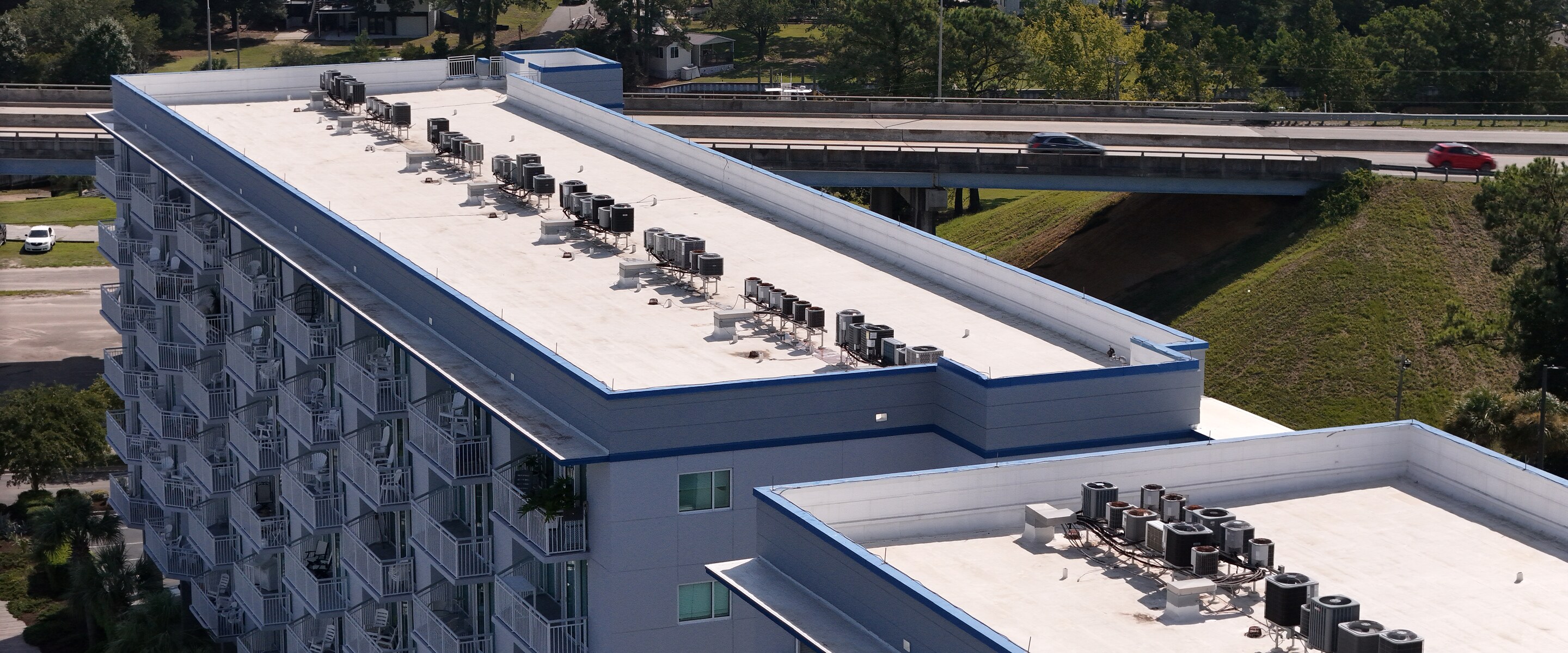 Aerial view of a multi-story commercial building with a white reflective roof coating and rows of rooftop HVAC units.
