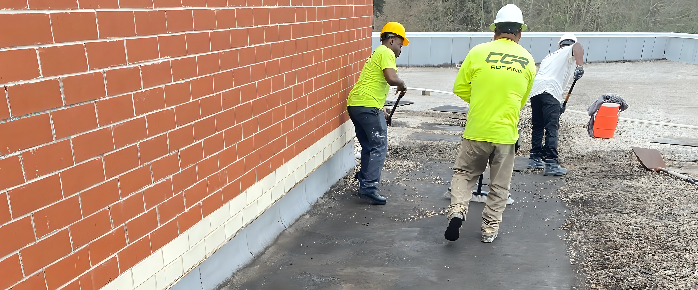 CCR Roofing crew clearing gravel and debris from a low-slope commercial roof during a built-up roof tear-off.