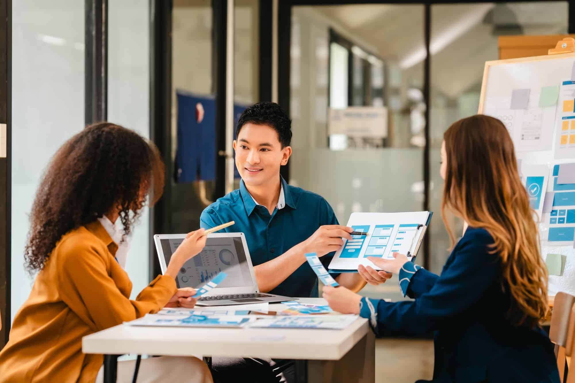 Diverse team of professionals engaged in a website graphic design board meeting, sharing opinions on UX and UI design elements. Asian man, African American people, black, afro, caucasian female
