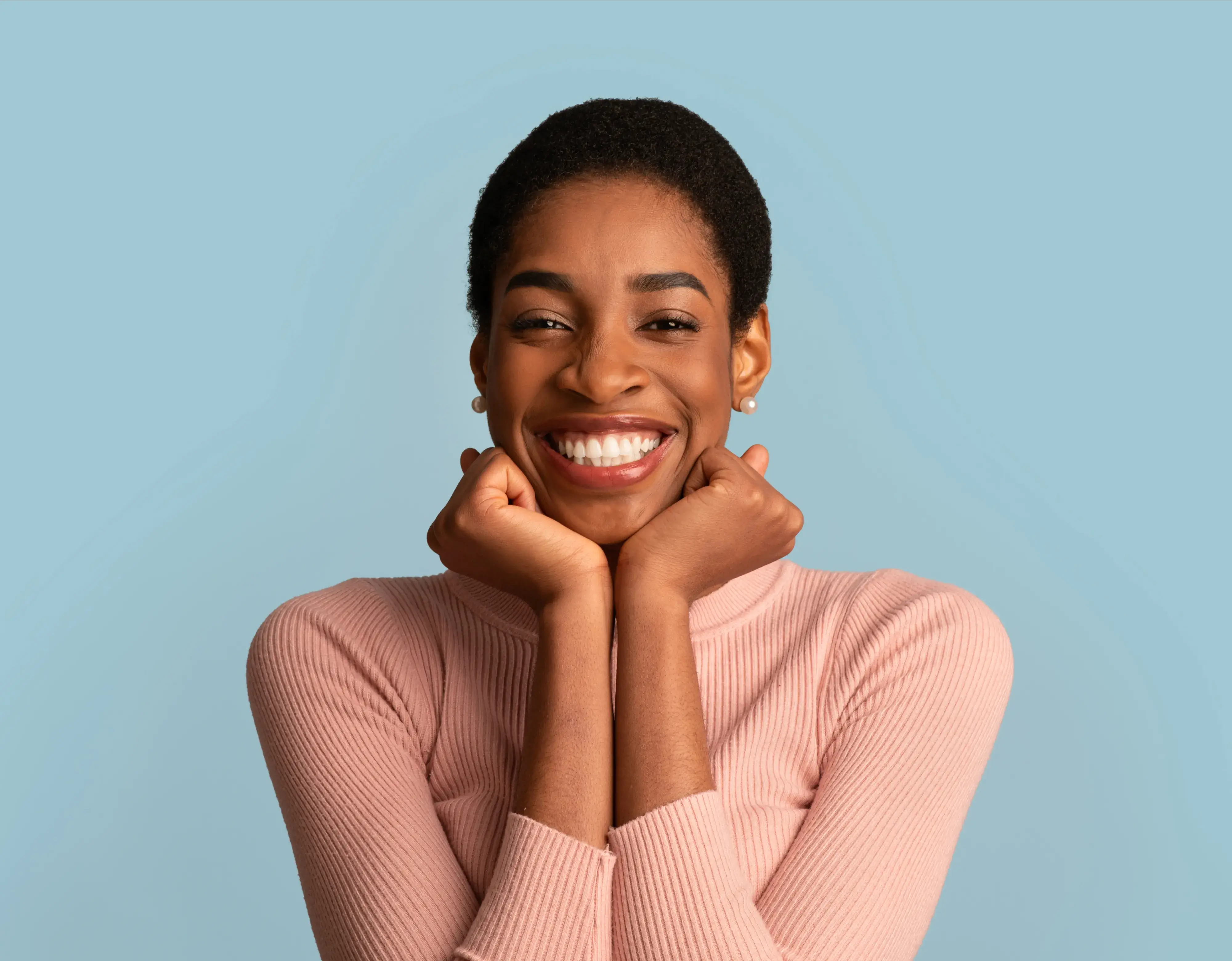 a girl is smiling for the camera in a pink sweater while leaning her chin to her left with an untidy blue background