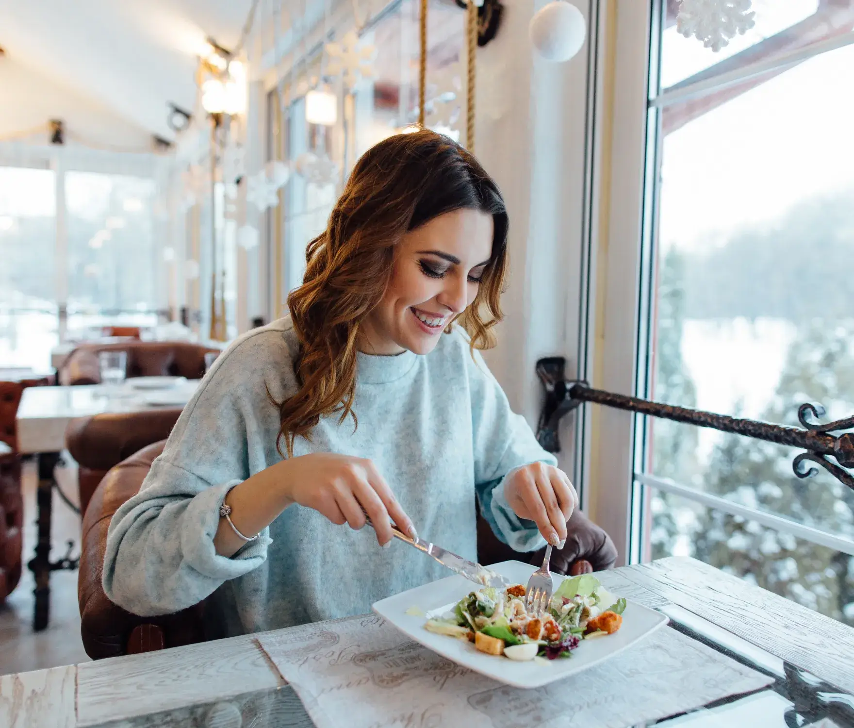 A woman smiles while eating a salad at a restaurant table.