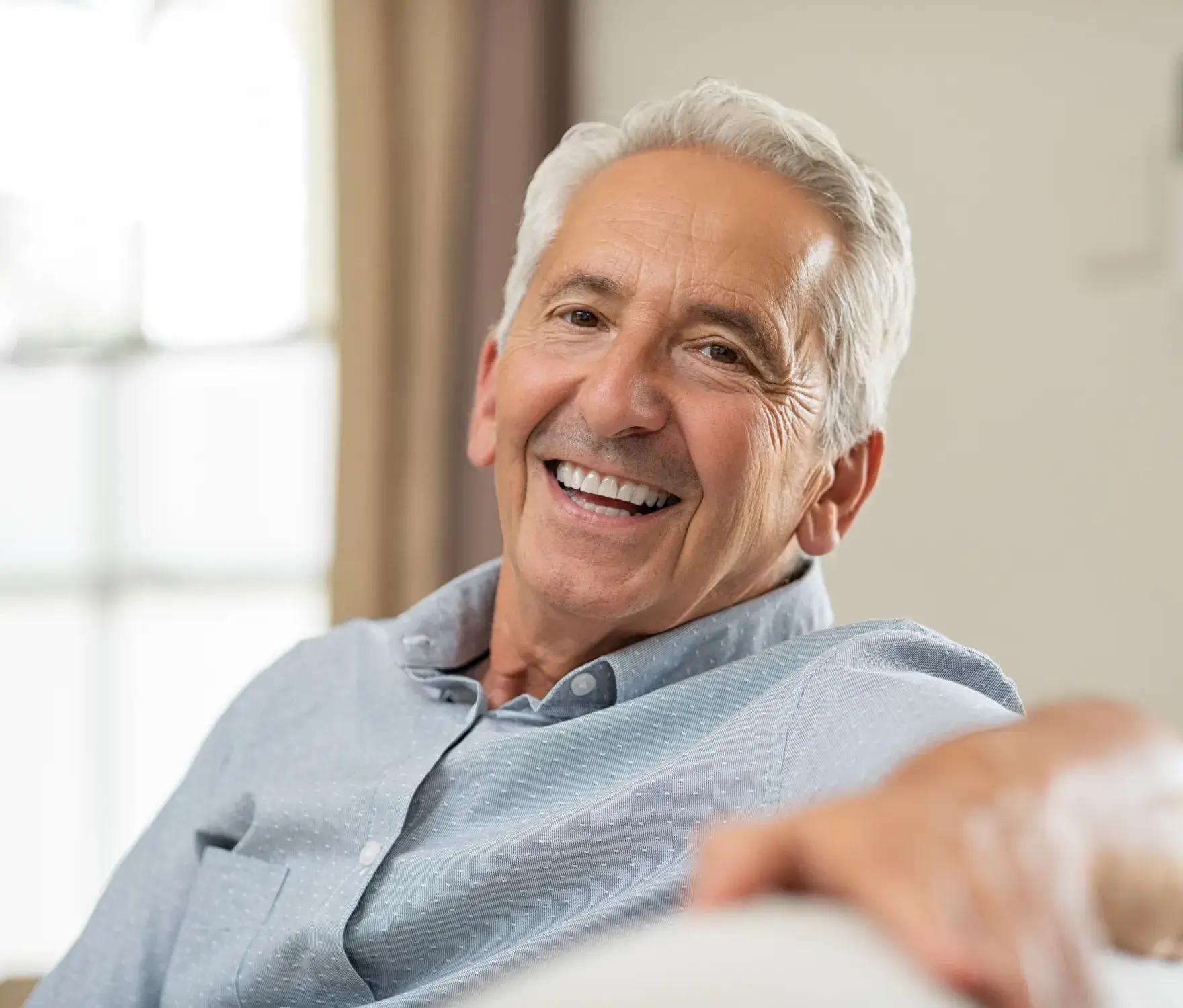 Older man with gray hair smiling while sitting indoors.