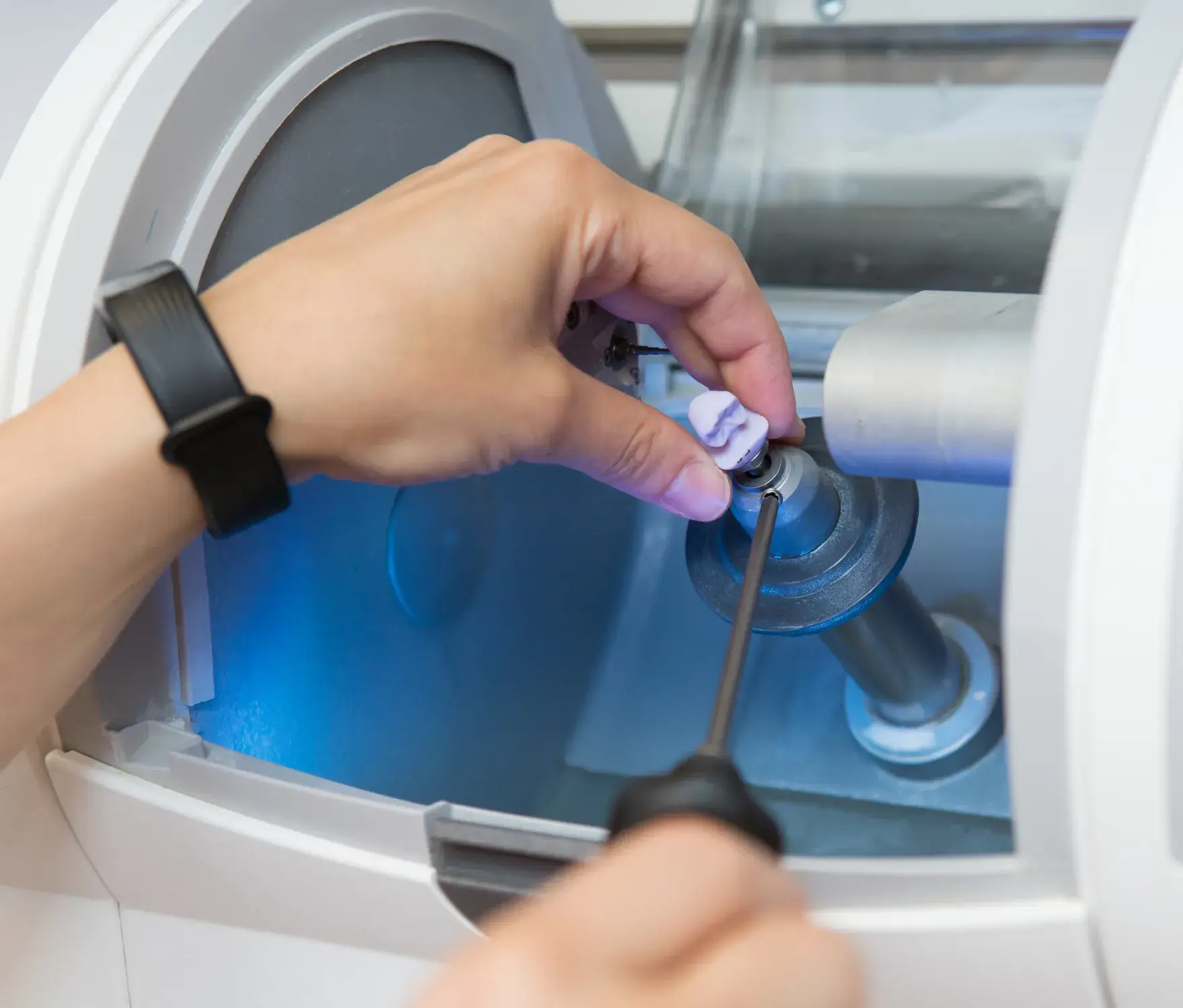 Close-up of a hand using a machine to carve a dental crown.