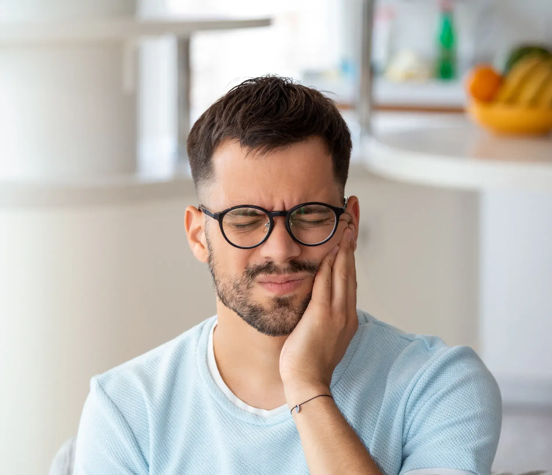 A man wearing glasses holds his cheek, appearing to be in pain or discomfort.