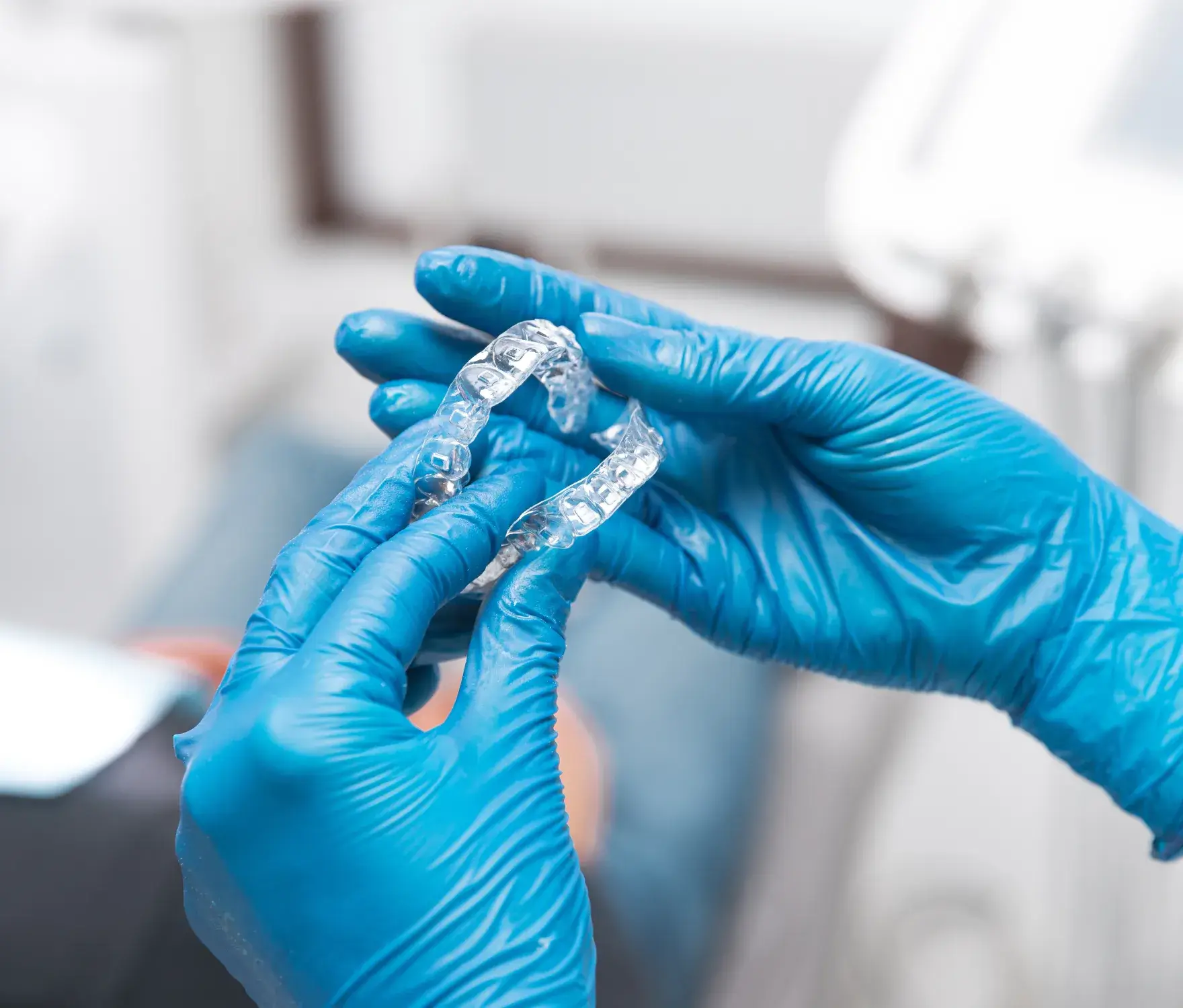 Two gloved hands holding a clear dental aligner in a clinical setting.