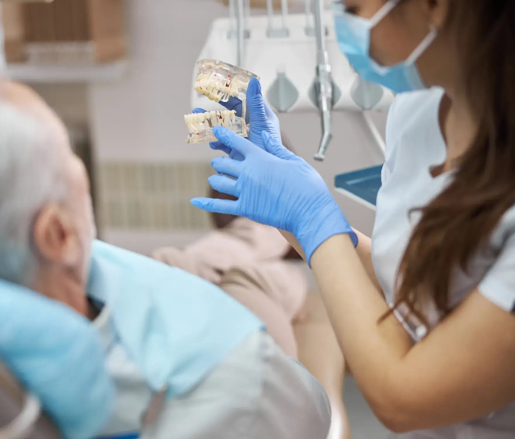 A dental professional shows an older patient a dental model while discussing treatment options.
