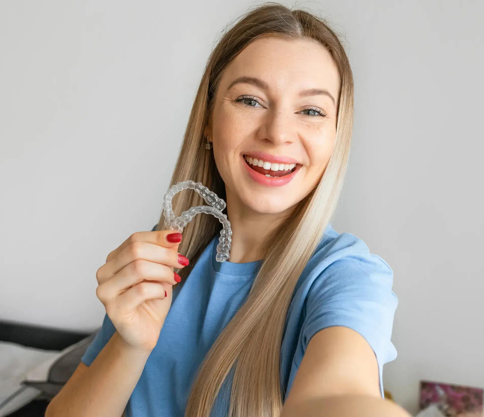 Smiling woman holding clear dental aligners in her hand.