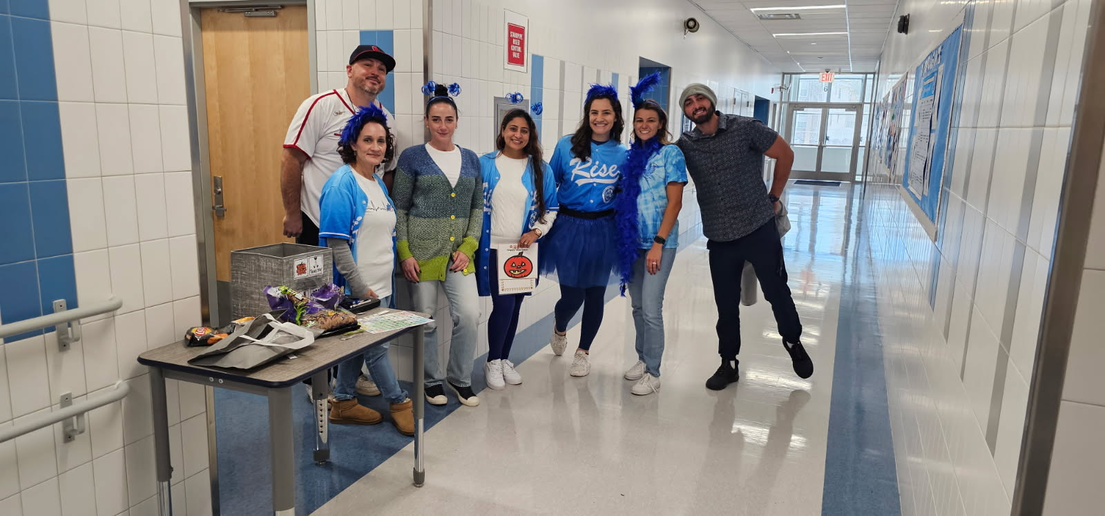 Staff members in blue costumes posing in school hallway on Halloween
