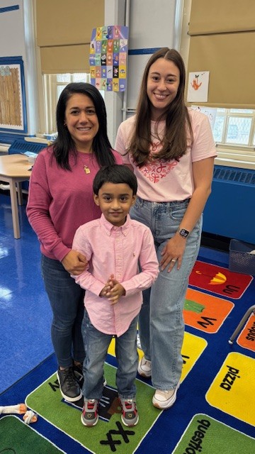 Two adults and a young student smiling together in a classroom