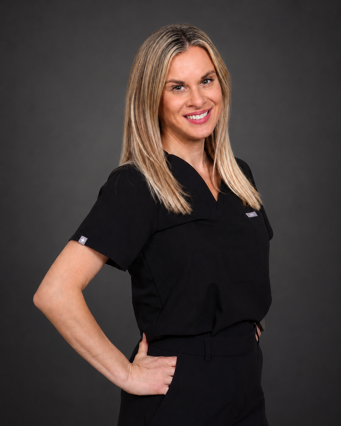 Smiling woman with blonde hair wearing black medical scrubs standing with hand on hip.