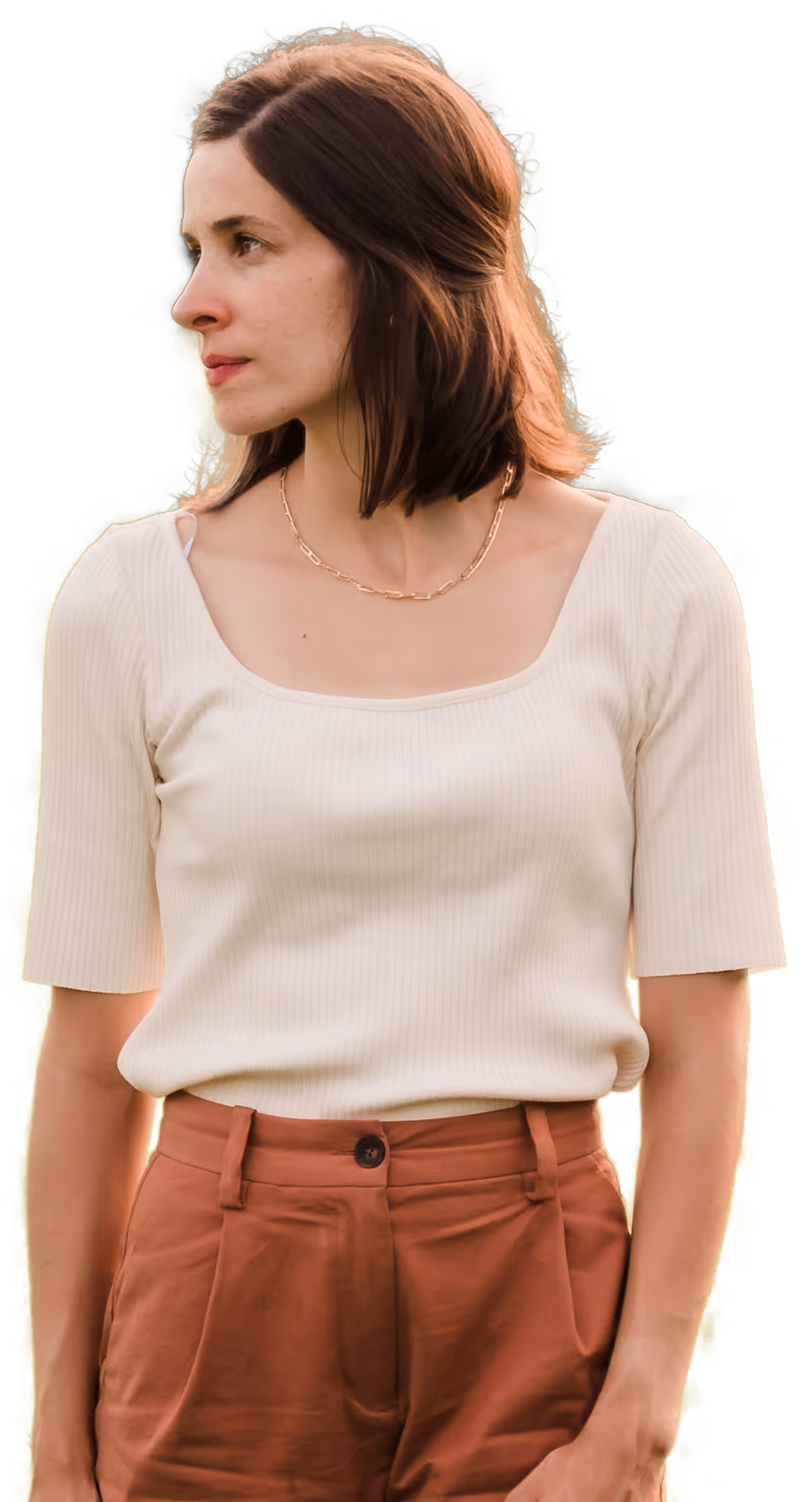 Femme aux cheveux bruns mi-longs, portant un haut crème à manches courtes et un pantalon brun rouge.