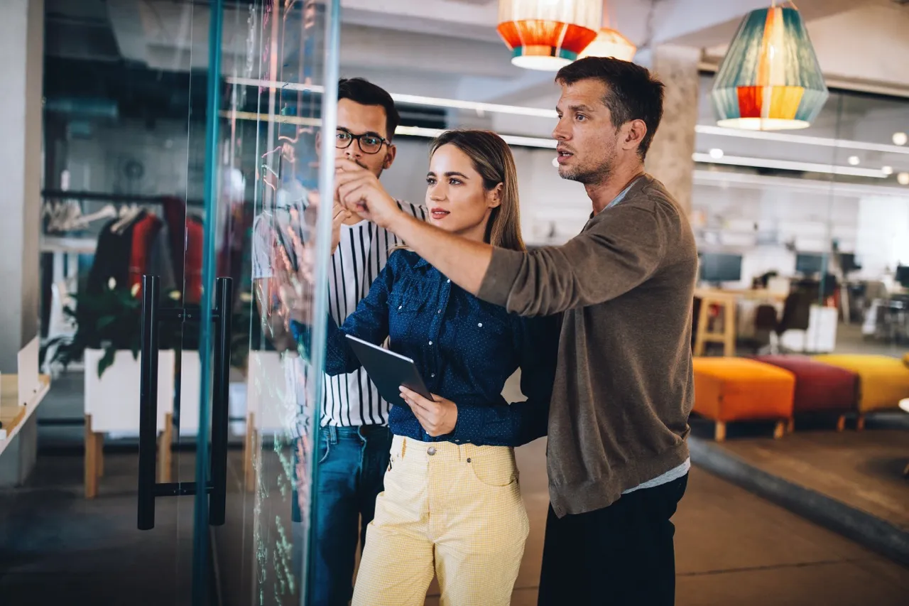 Group brainstorming around glass wall writing notes