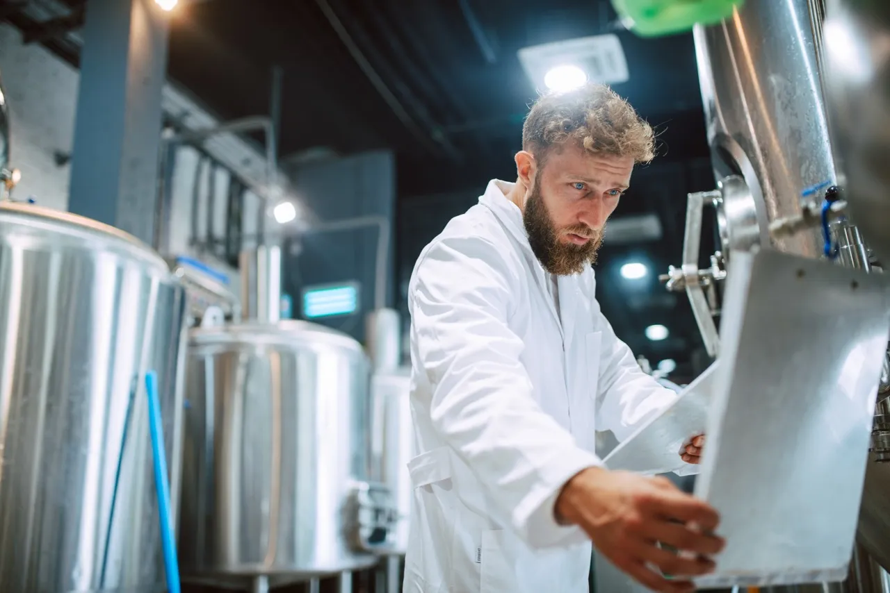 Man in lab coat checking papers on large containers