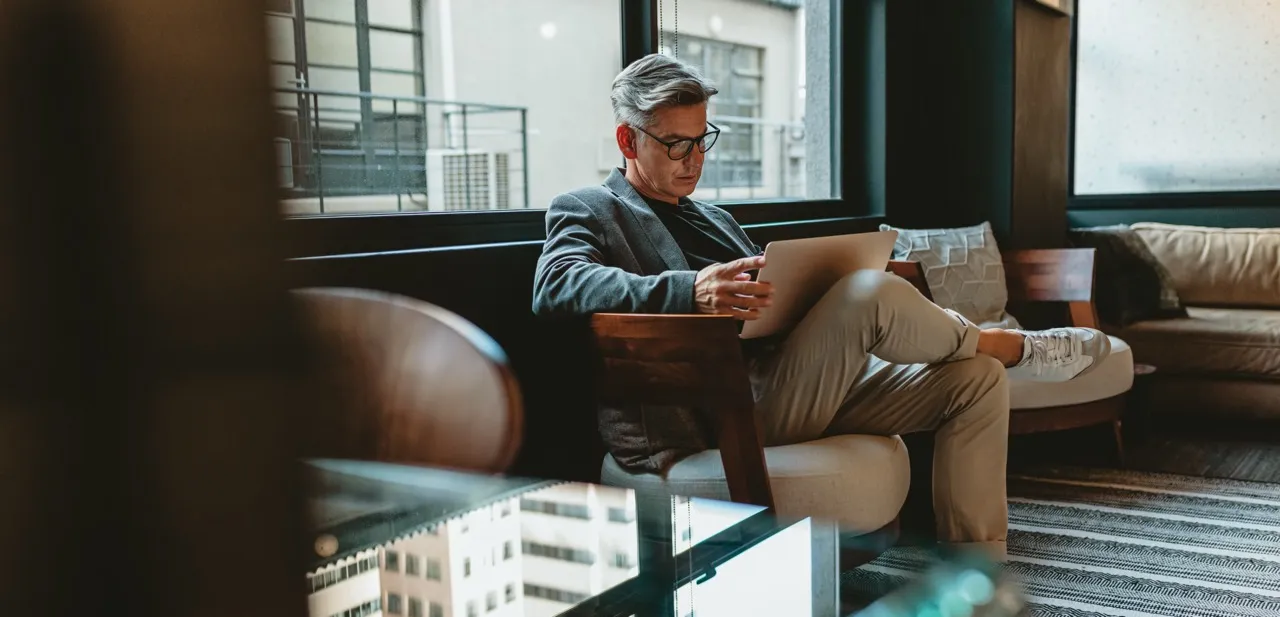 man well-dressed sitting in a chain reading his laptop