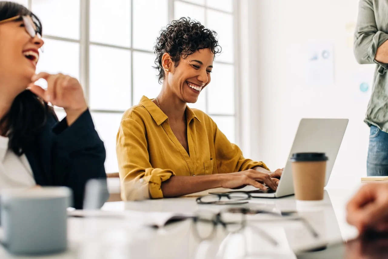 two women working at a table laughing with their computers and coffee on the table