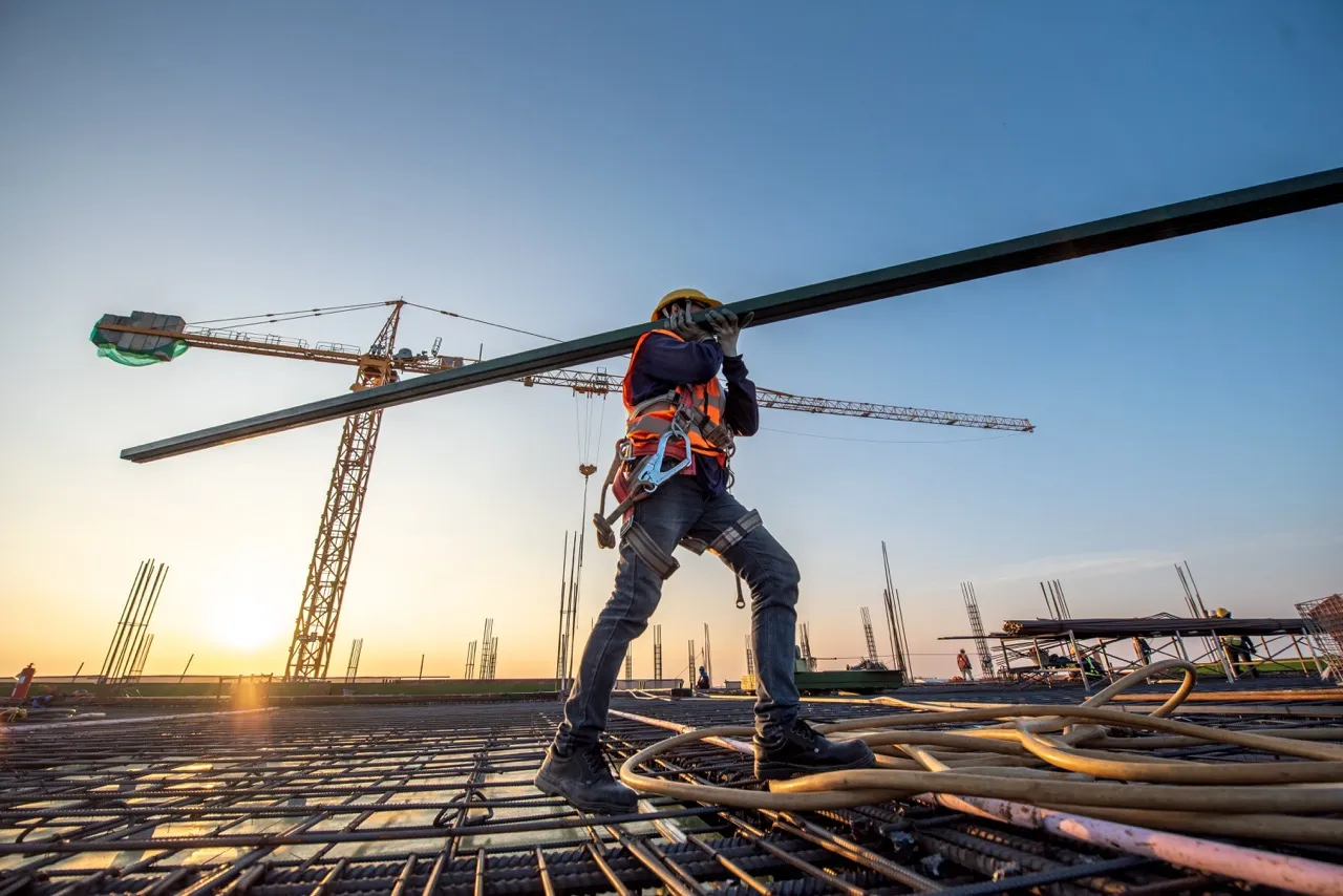 Construction worker carrying a beam across a work site