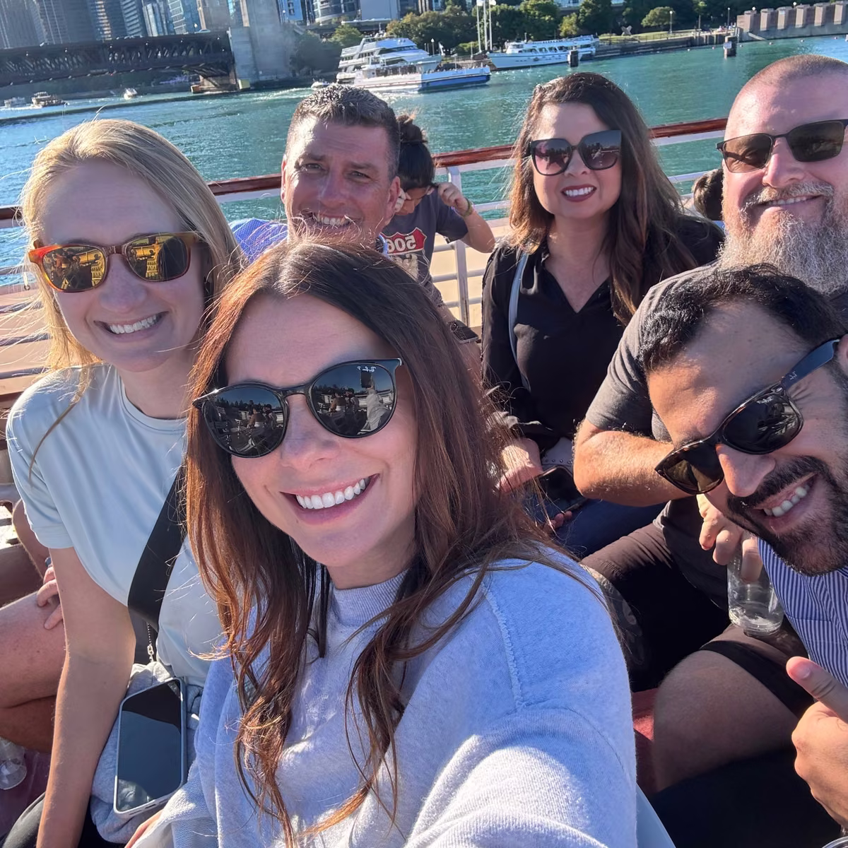 Chicago river outing with six colleagues in sunglasses smiling for a group selfie on a boat.