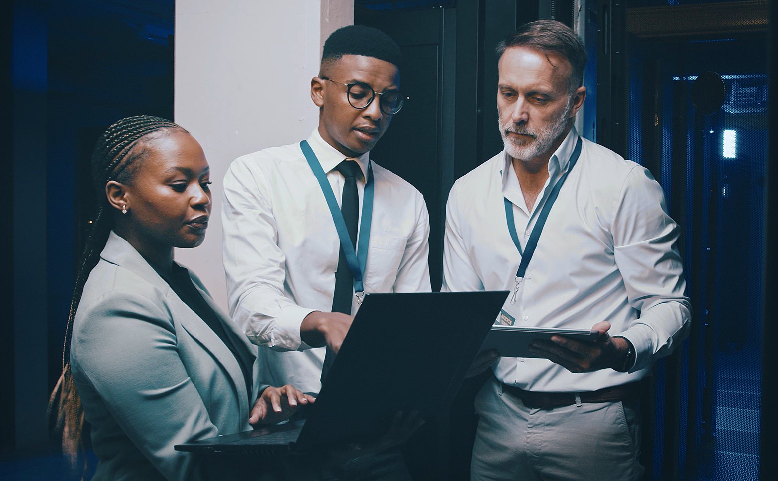 team of three in a server room collaborating on laptop and tablet