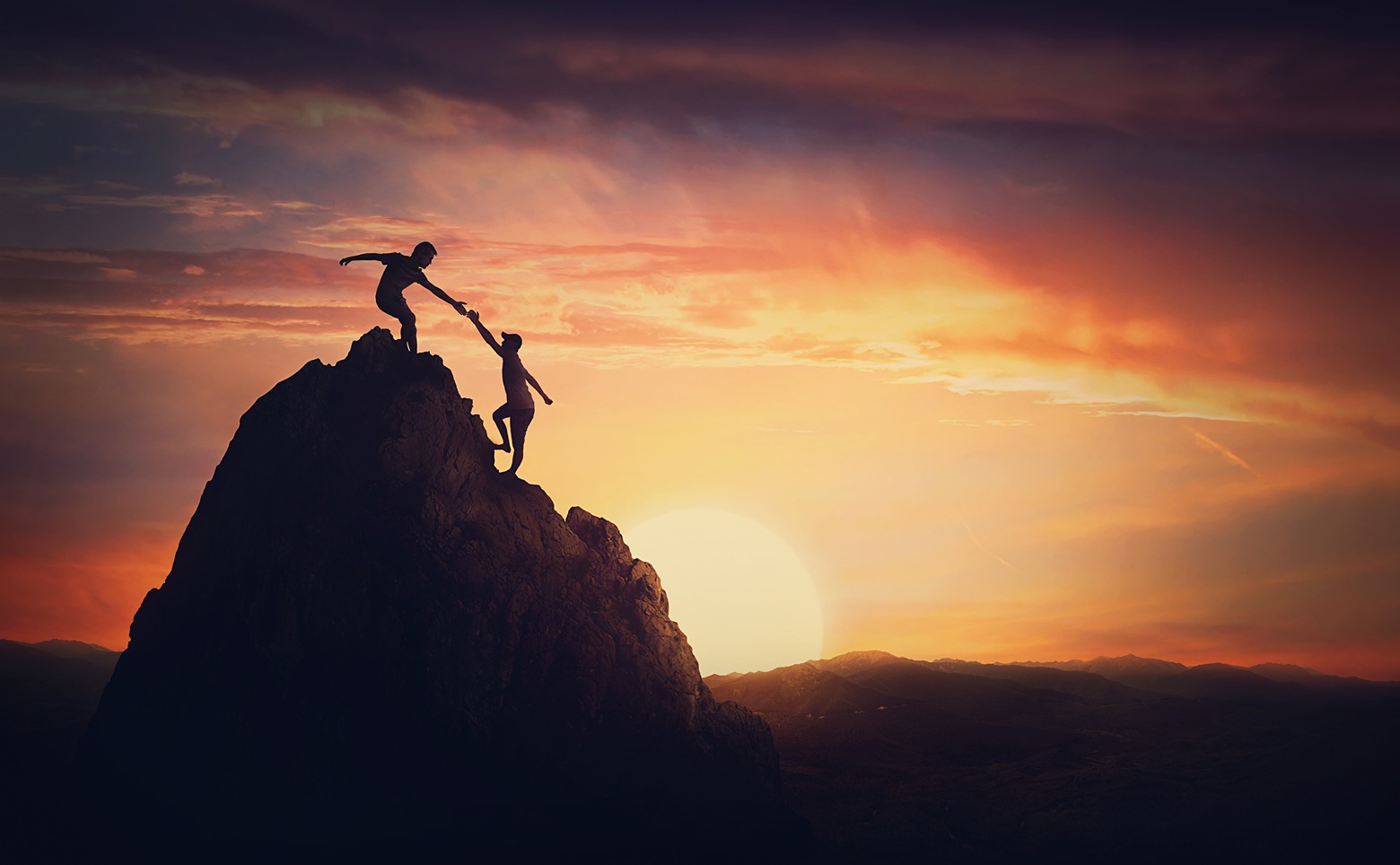 Scenery view with a team of two climbers on the top on the mountain. Person helping another to overcome obstacles and reach the top together. Teamwork to achieve success
