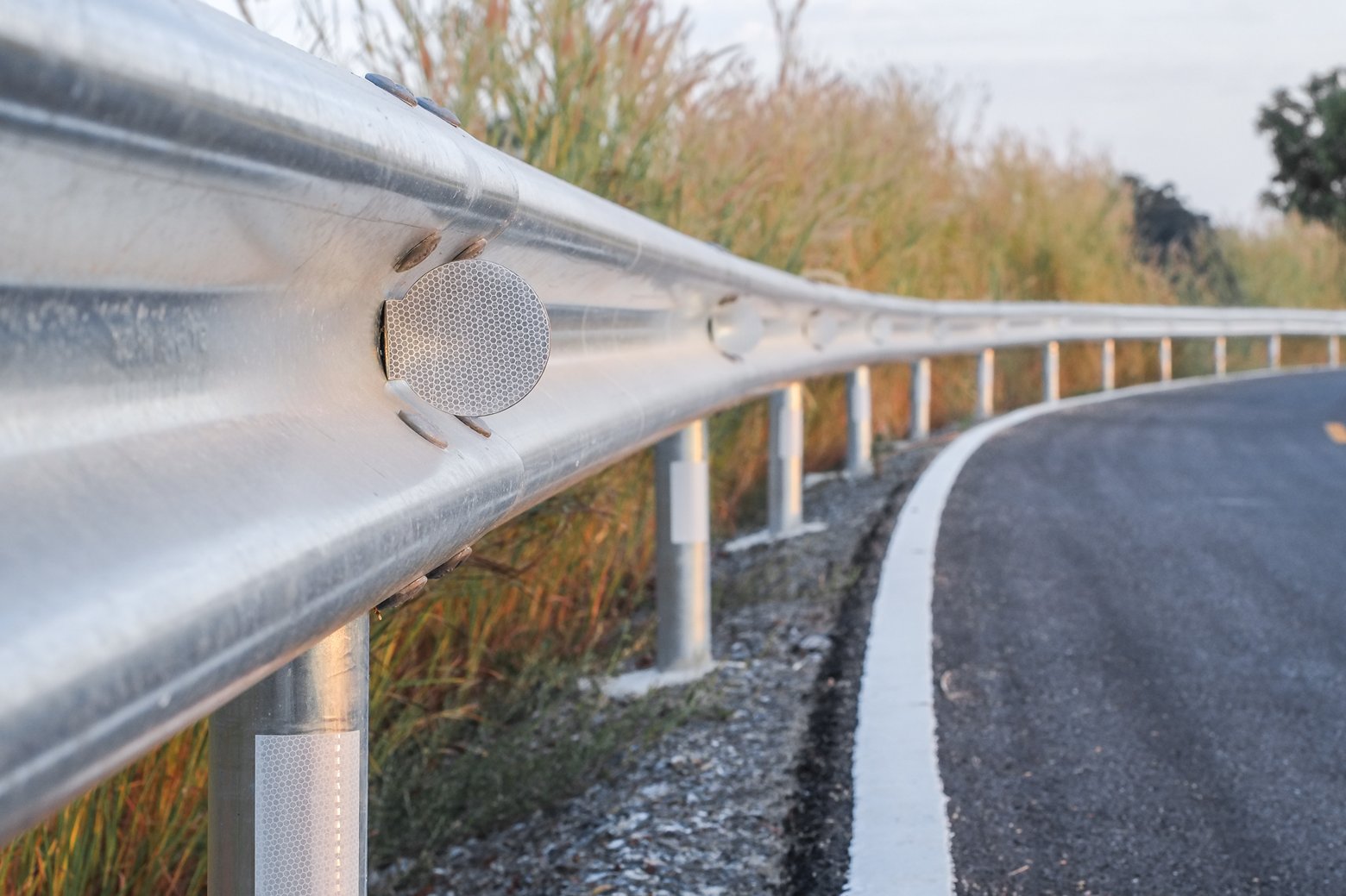 Close-up of a metal guardrail with reflectors running alongside a curving road