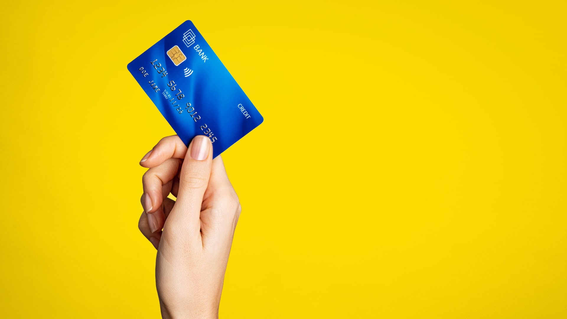 Yellow background, hand holding up a blue credit card