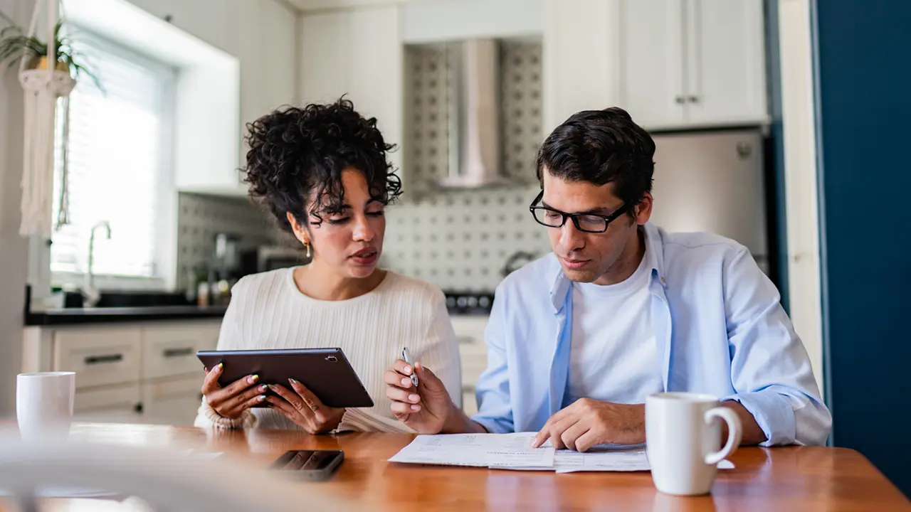 A couple reviewing a budget on a laptop with a notepad and calculator nearby, representing practical money management strategies for financial health.
