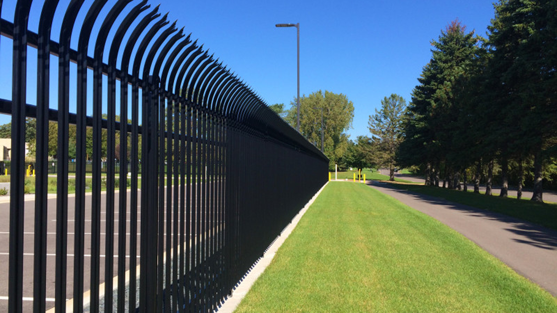 A view of an iron fence on the perimeter of a property surrounded by trees and grass.