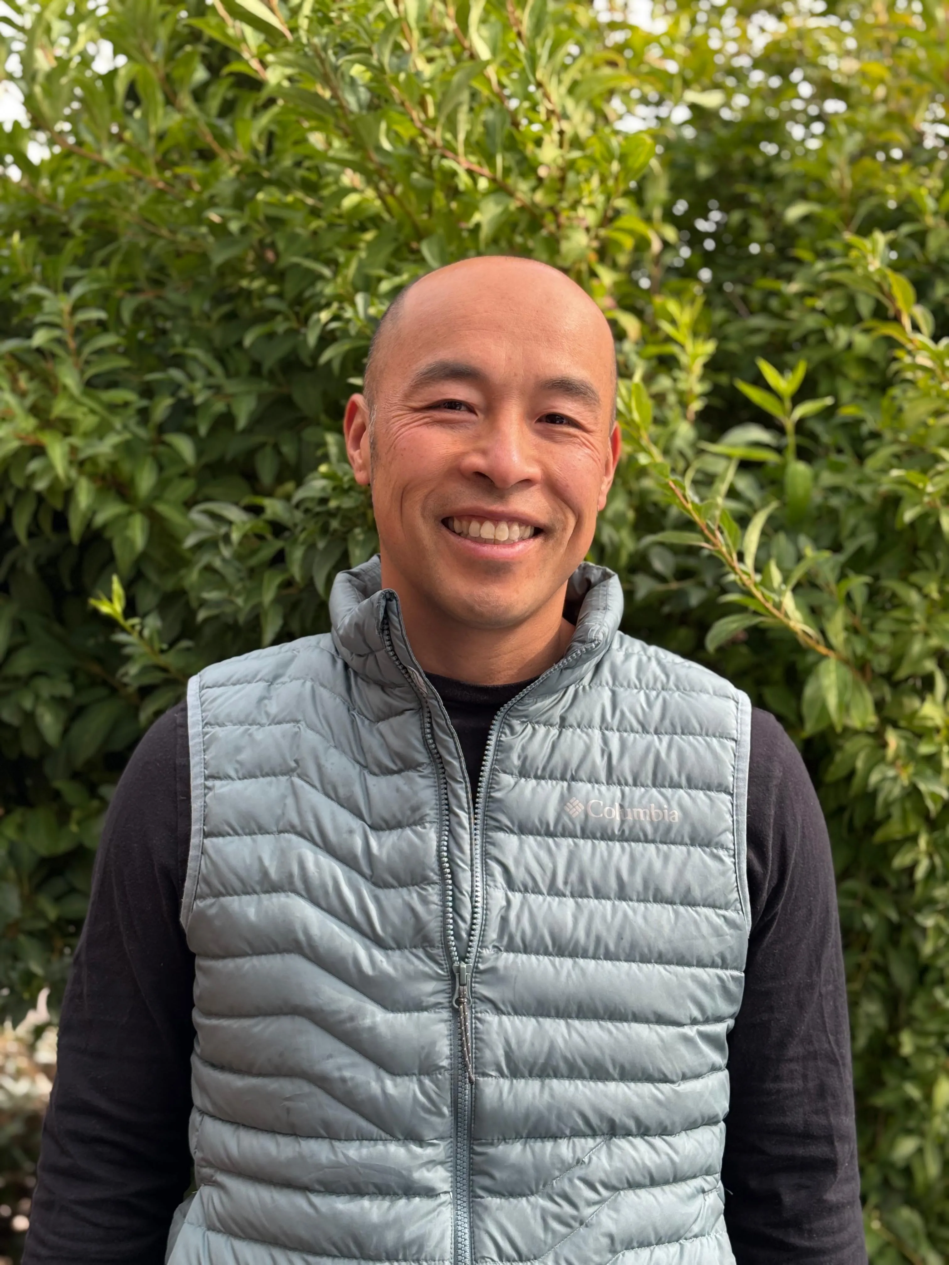 headshot of asian man, no hair, wearing a light blue vest