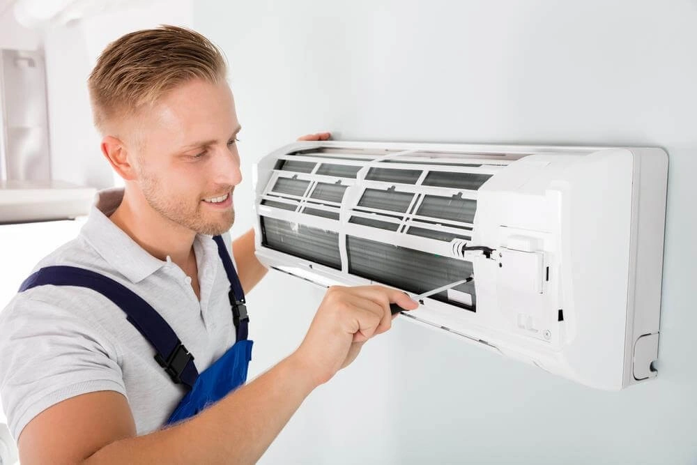 Smiling technician maintaining wall-mounted AC unit.