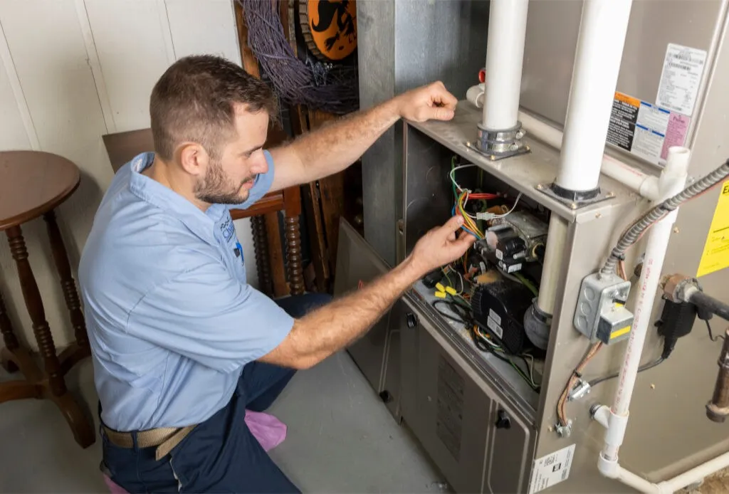 Repairman adjusts wiring inside a furnace.