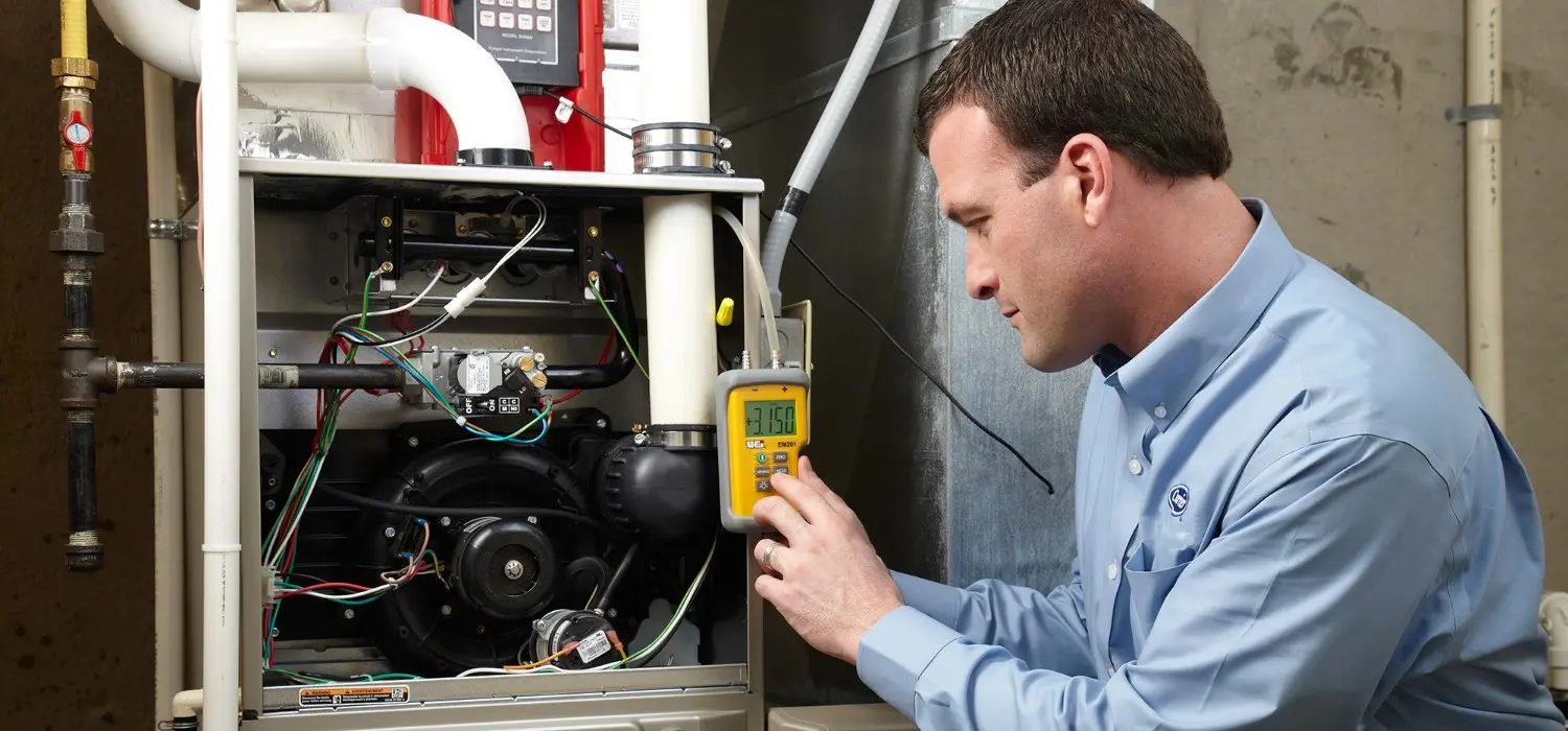 Technician measures furnace pressure with manometer tool.