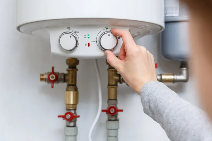 Person adjusting the temperature and flow control knobs on a tankless water heater.