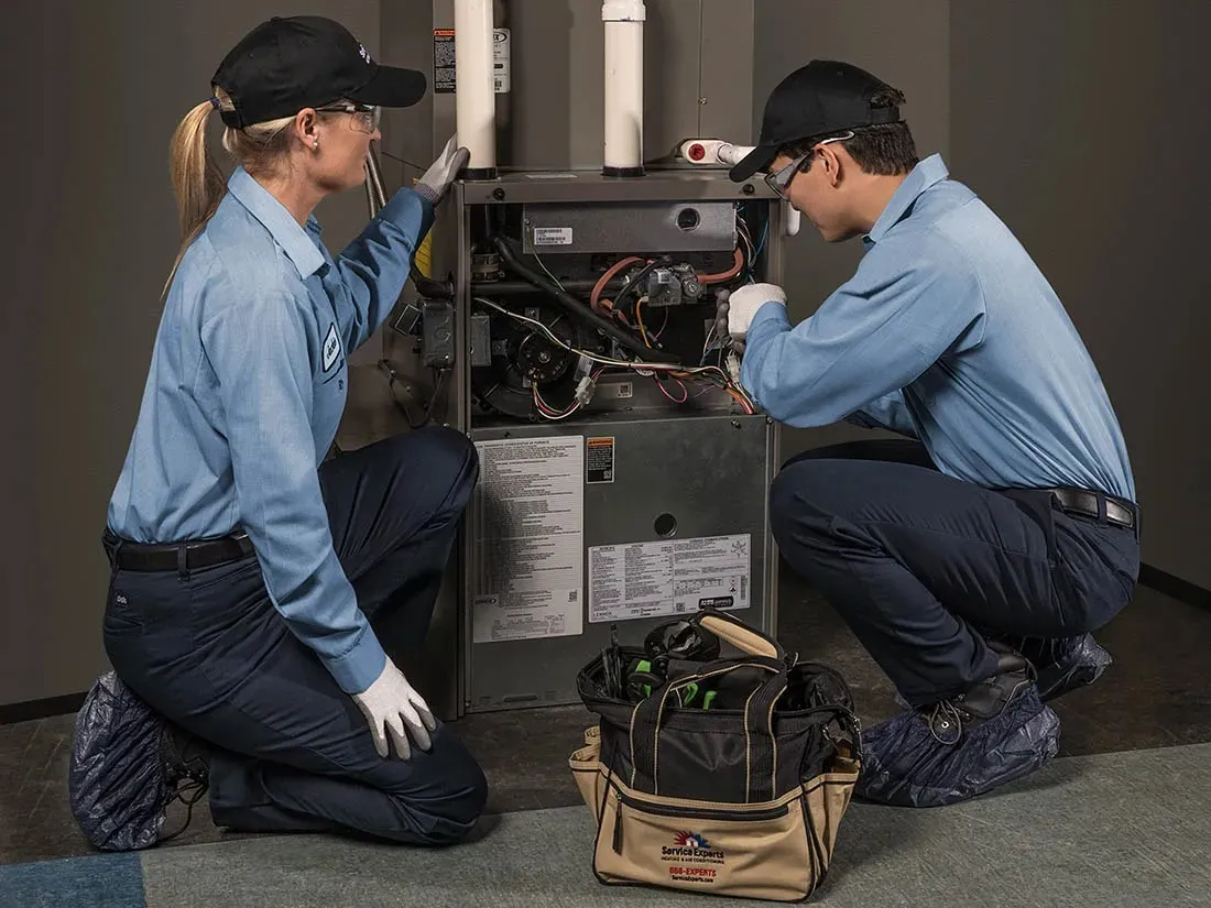 Two technicians repair an open furnace.