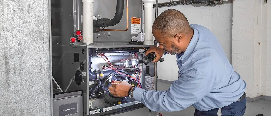 Technician inspects furnace with flashlight and tools.