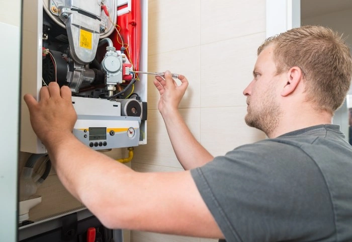 Plumber repairs small wall-mounted boiler.