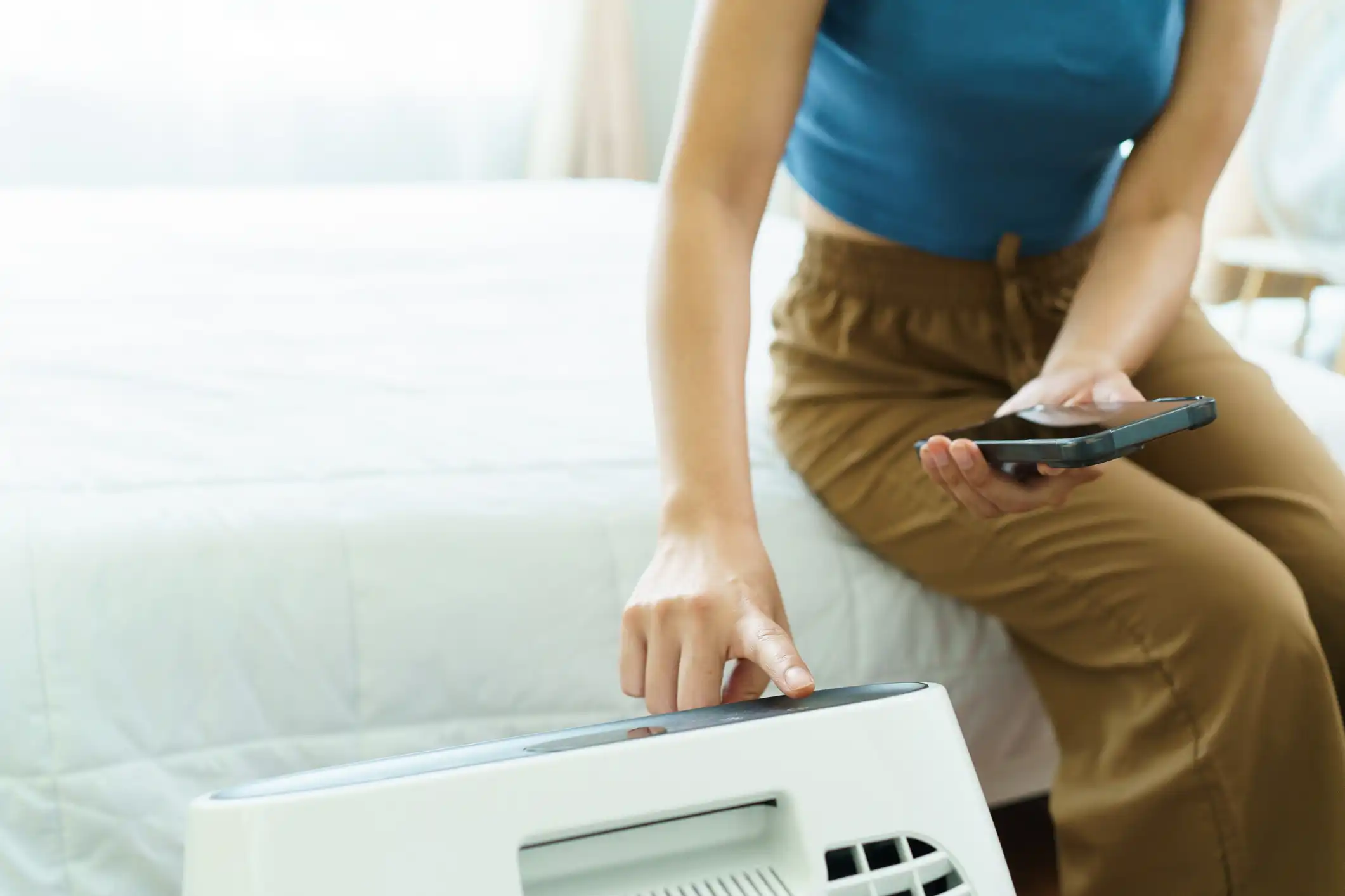 Close-up of a person's hand adjusting a device, possibly a heater or air purifier, in a bedroom.
