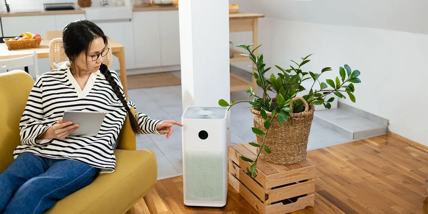 Woman monitors air purifier with tablet.