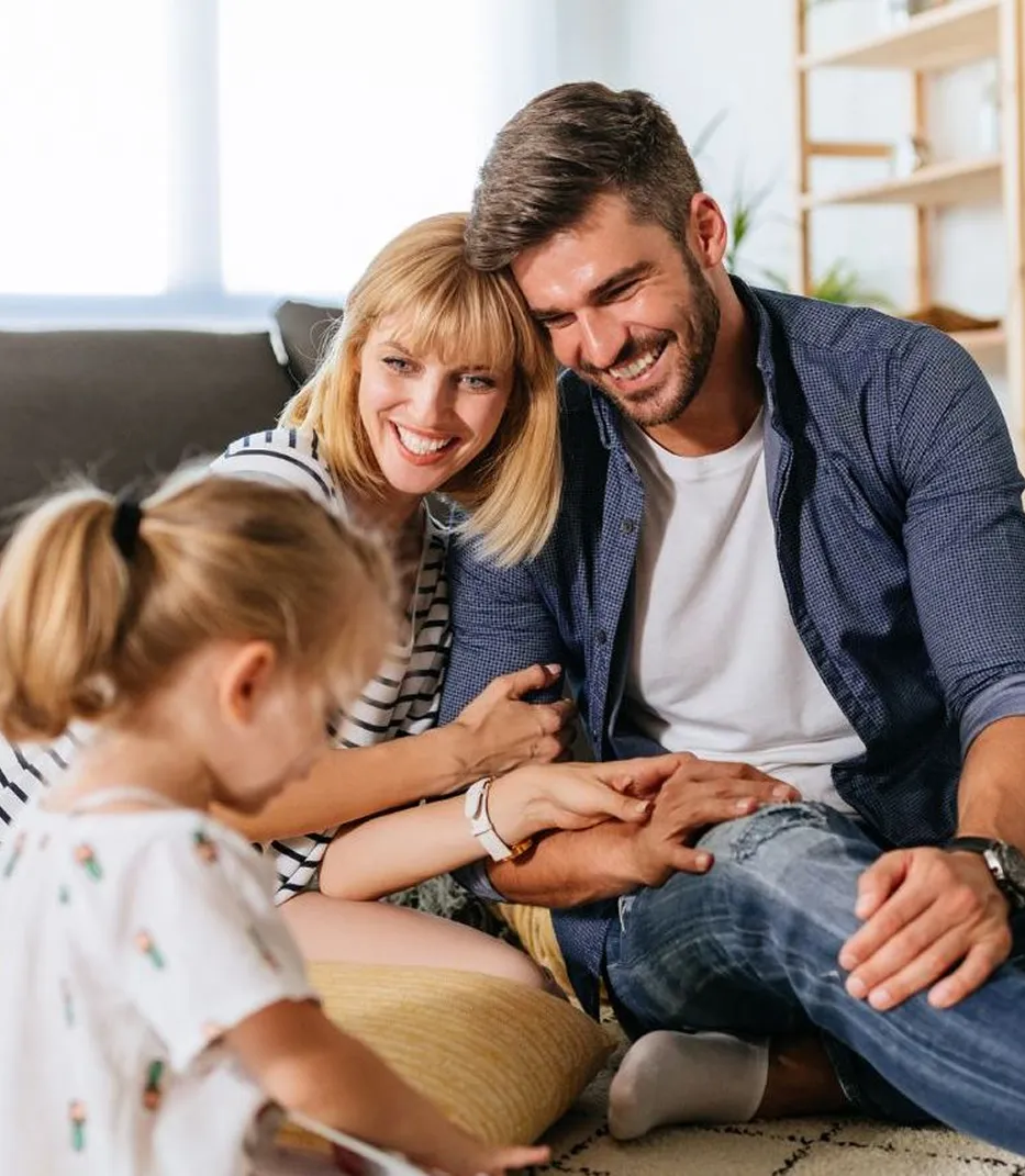 Happy family cuddling together on couch, smiling and holding hands