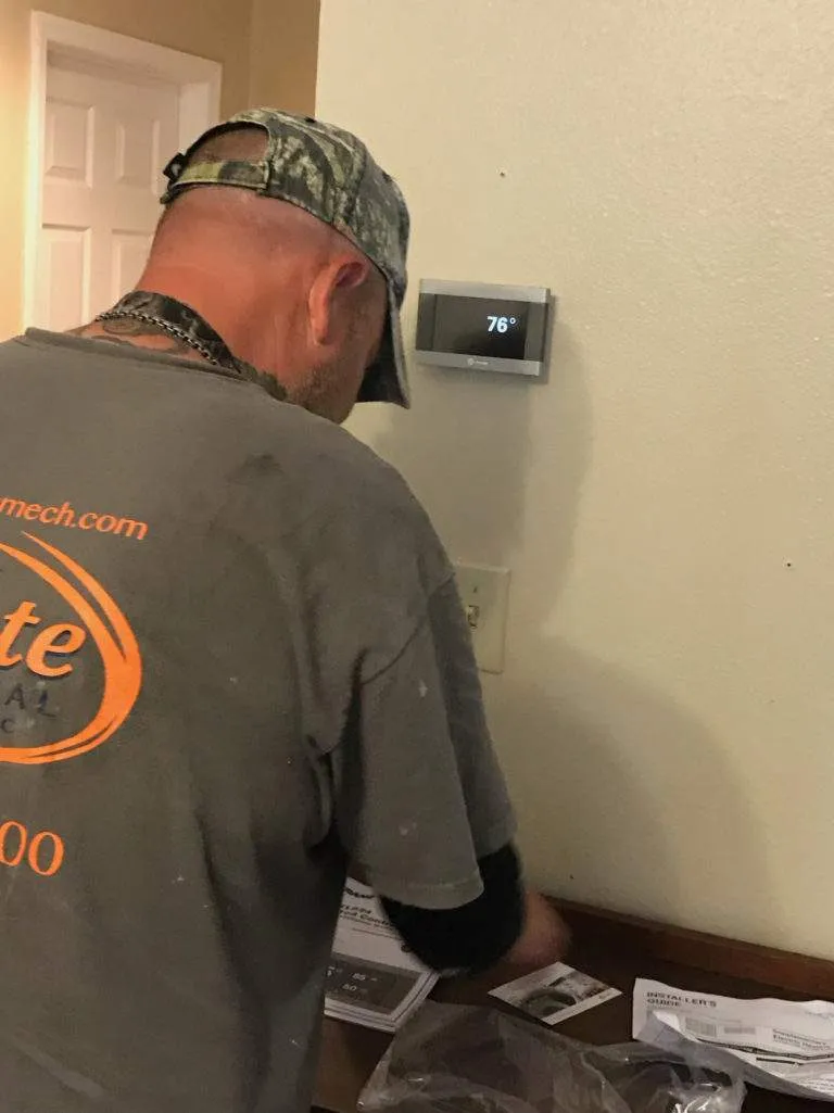 Technician in camouflage hat checking thermostat at 76 degrees