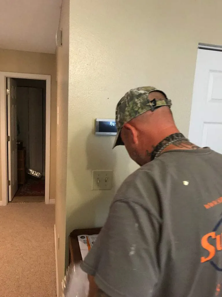 Worker in camouflage cap checking thermostat in hallway