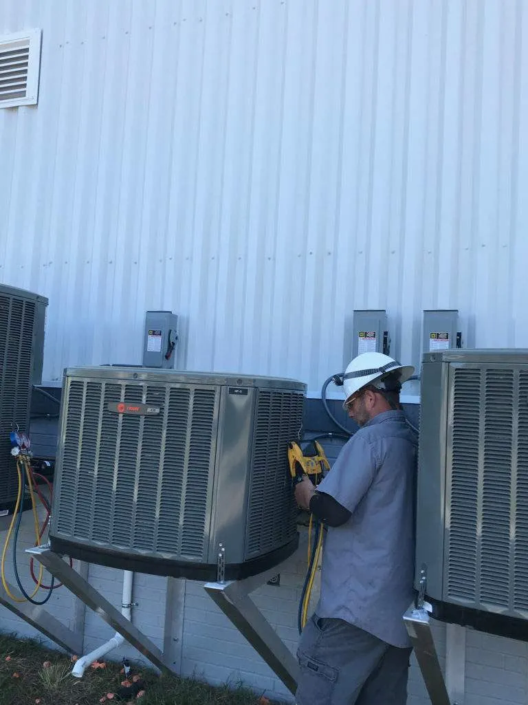 HVAC technician in hard hat checking air conditioning units outside building