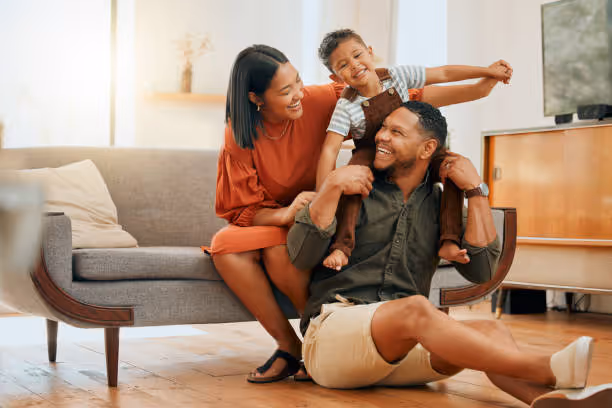 Happy family playing together on living room floor, child on parent's shoulders
