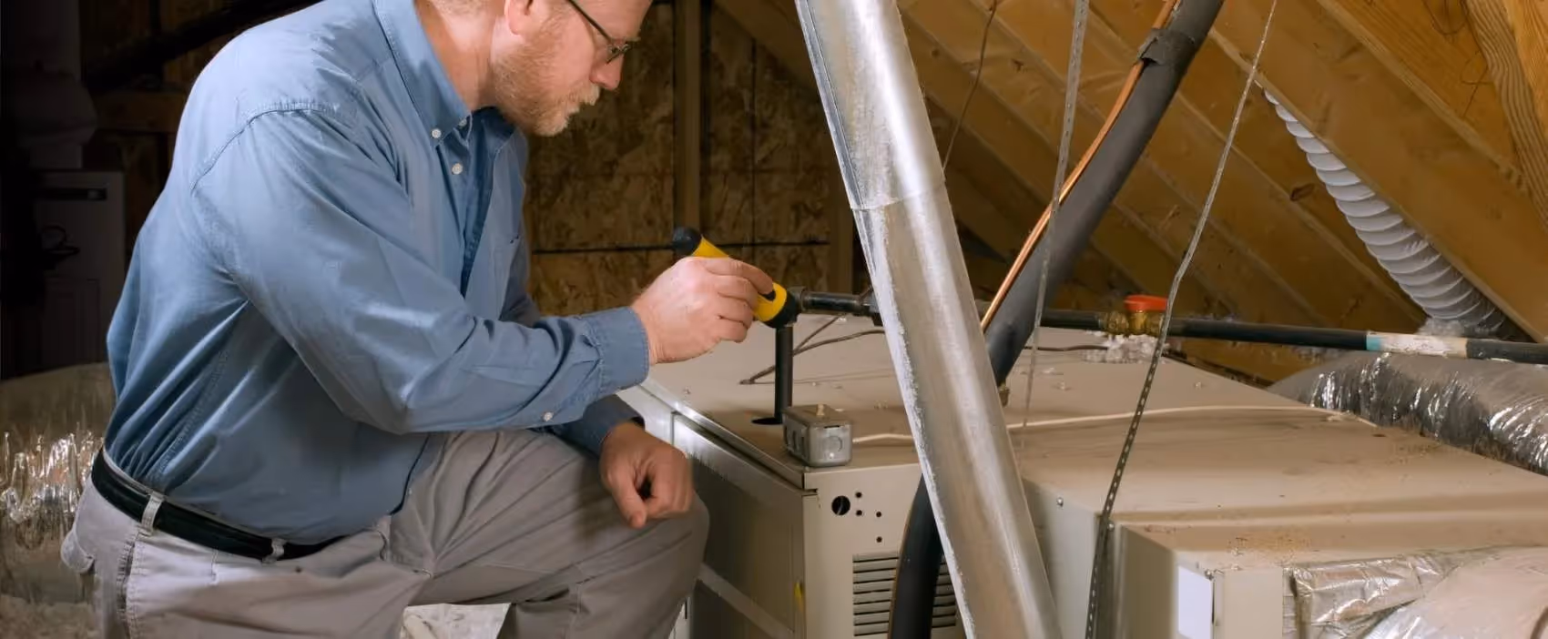 Technician inspecting HVAC system in residential attic with tools