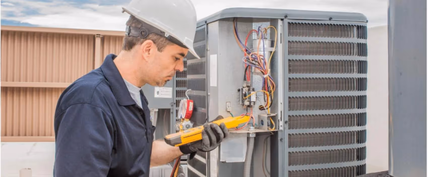 Technician in hard hat checking HVAC unit with electrical testing device